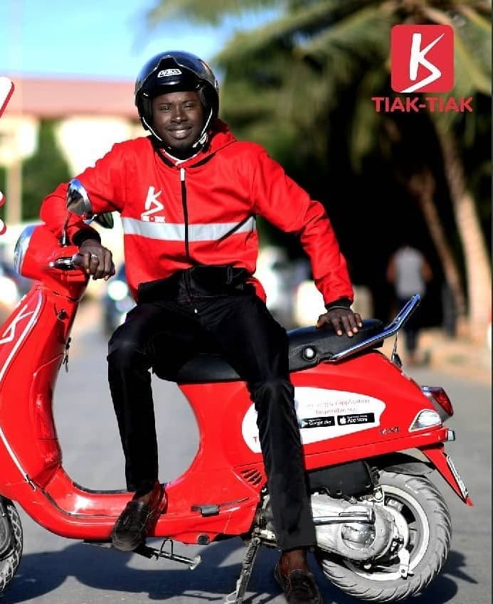 Un livreur Tiak-Tiak sur sa Vespa rouge, dans une rue de Dakar